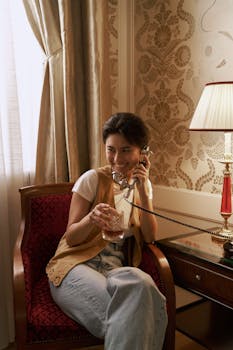 A woman sits in a luxurious room, talking on a vintage phone, exuding a retro vibe.
