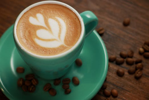 Close-up of a green coffee cup with delicate latte art, on a wooden table.