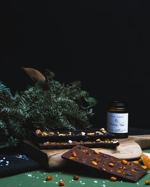 Free A gourmet dark chocolate bar adorned with nuts and exotic spices on a wooden board beside aromatic pine leaves. Stock Photo