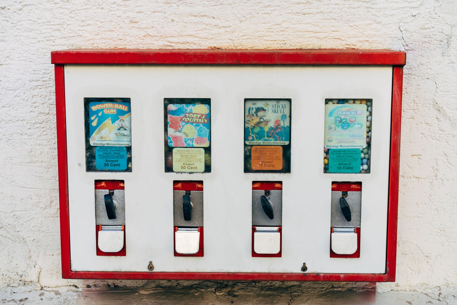 Close-up of a vintage vending machine for gum and candy on a textured white wall.