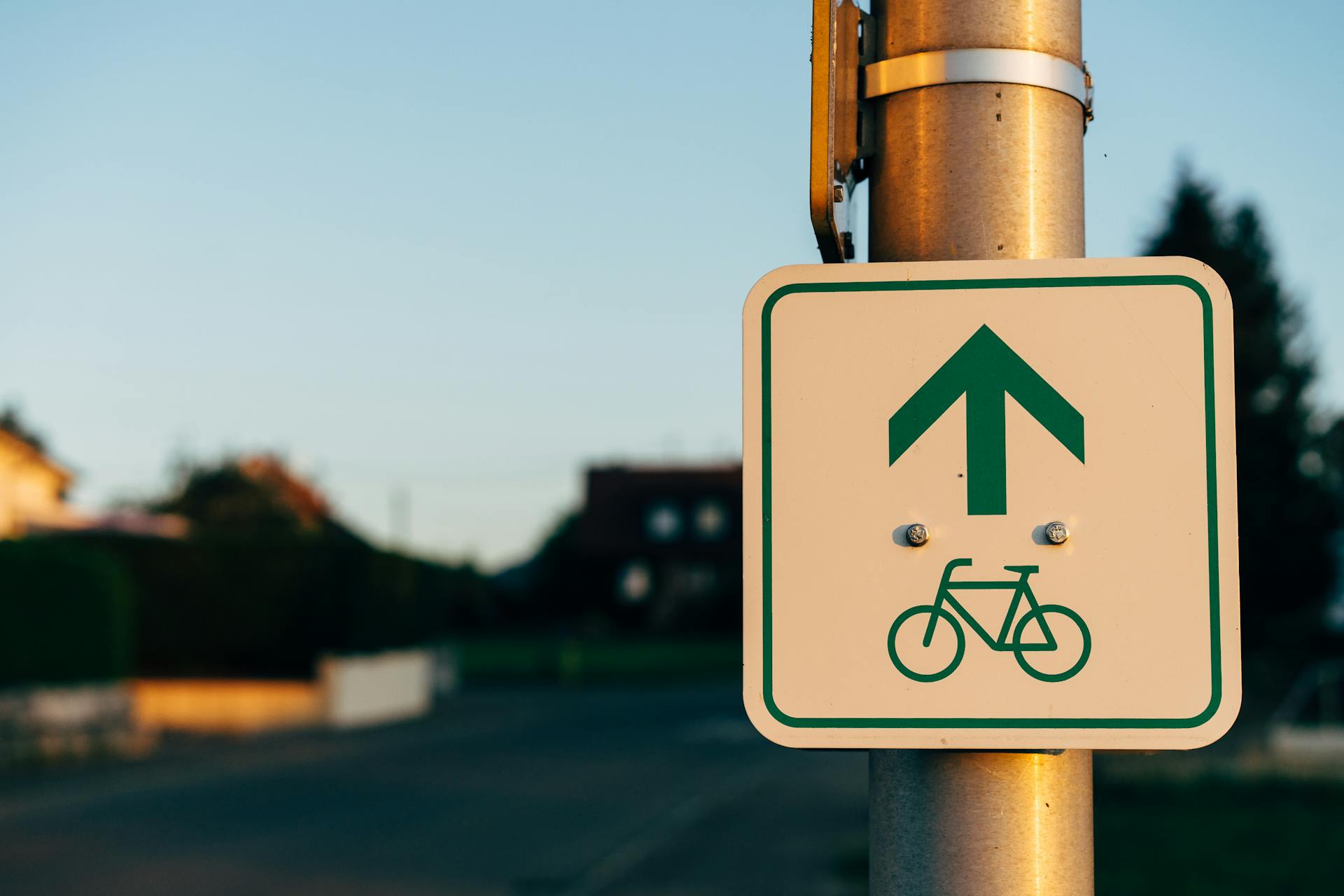Close-up of a bicycle lane sign on a metal post during sunset, indicating cycling direction.