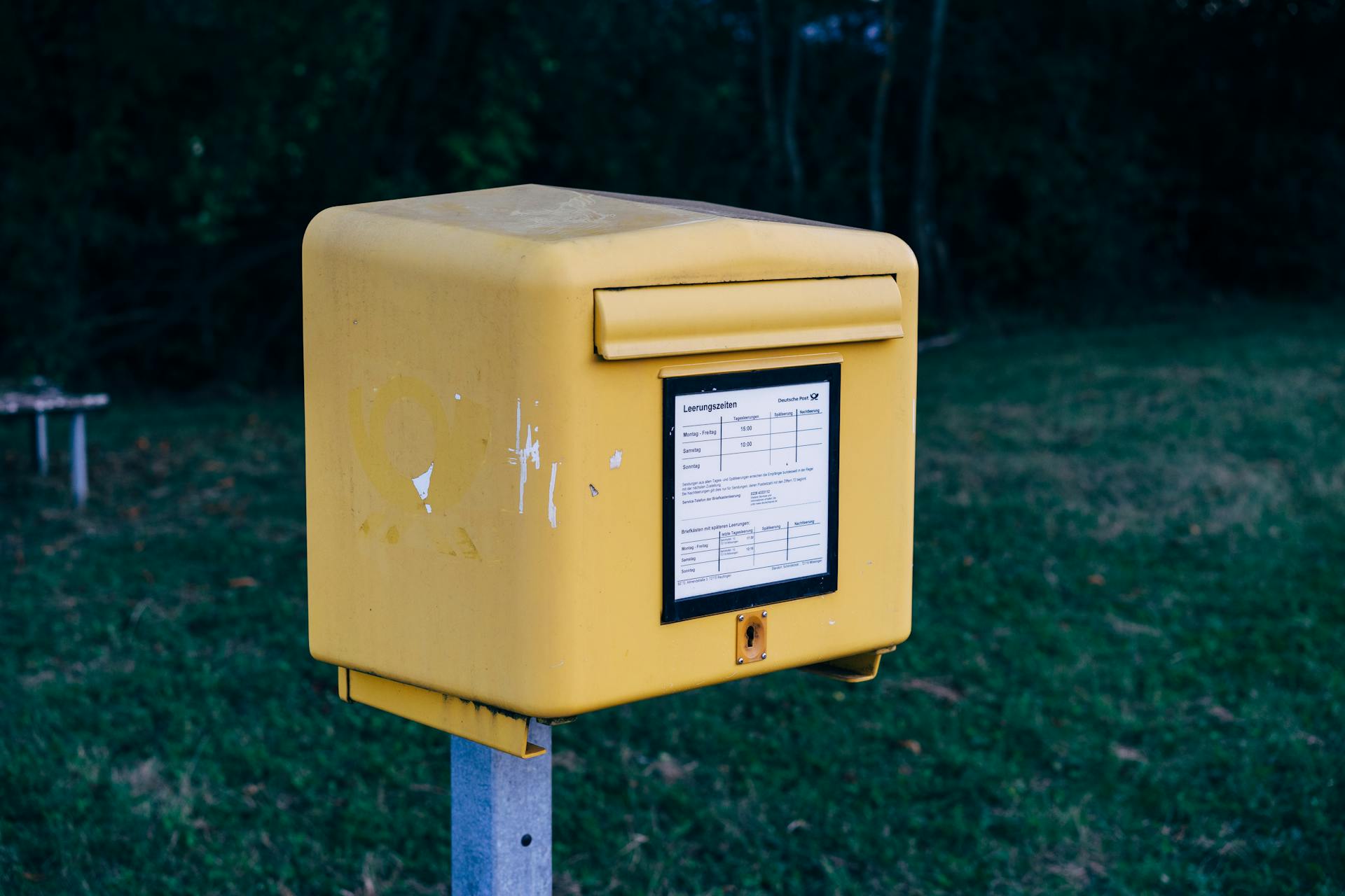 A yellow mailbox stands on green grass in an outdoor area.
