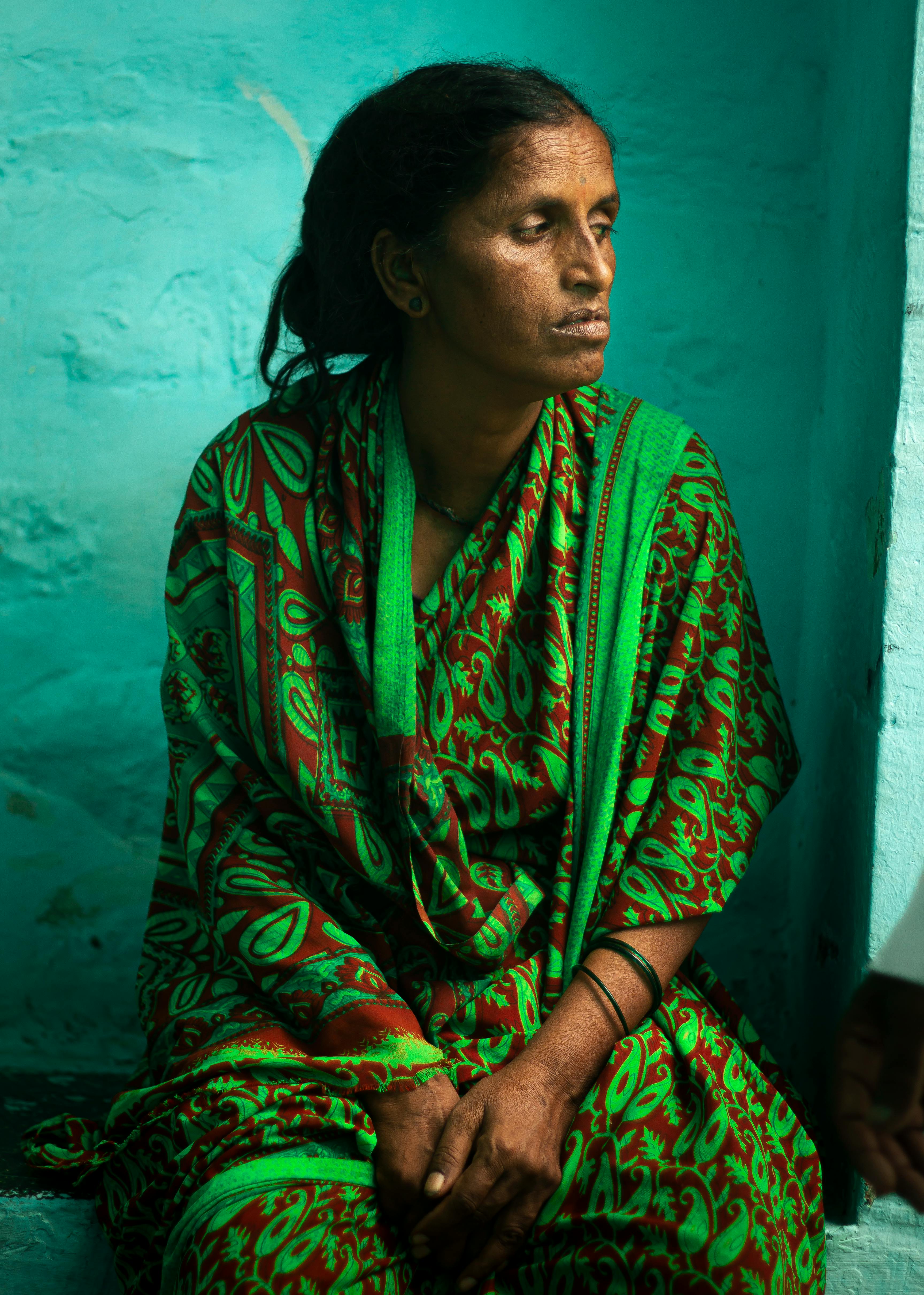 Expressive portrait of a woman in a green sari against a vivid teal wall.
