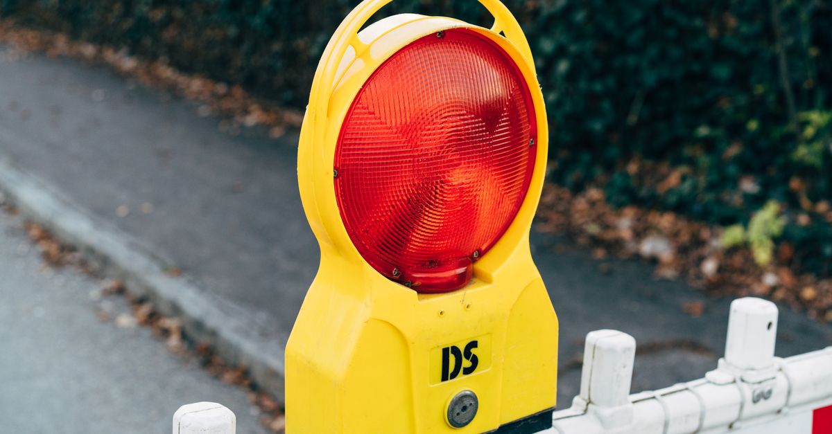 Close-up of a red warning light on a road construction barrier during autumn.