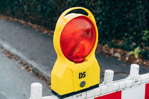 Close-up of a red warning light on a road construction barrier during autumn.