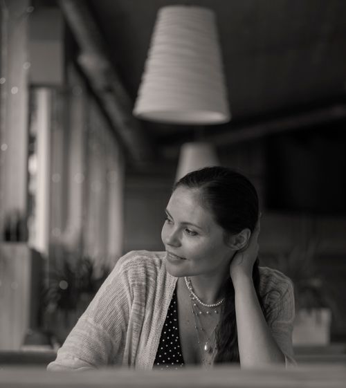 Free A contemplative woman seated indoors, bathed in soft light, in a stylish cafe setting. Stock Photo