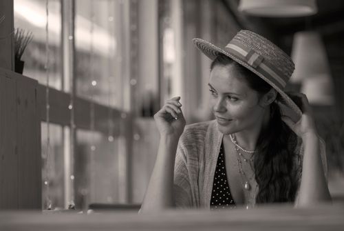 Free Black and white portrait of a smiling woman in a straw hat and pearl necklace indoors. Stock Photo