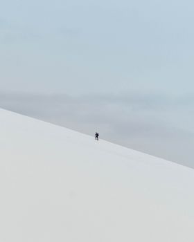 A lone hiker ascends a snowy slope in Norway's remote wilderness, showcasing winter adventure.