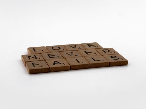 Scrabble tiles arranged to spell 'Love Never Fails' on a clean white background, symbolizing enduring love.