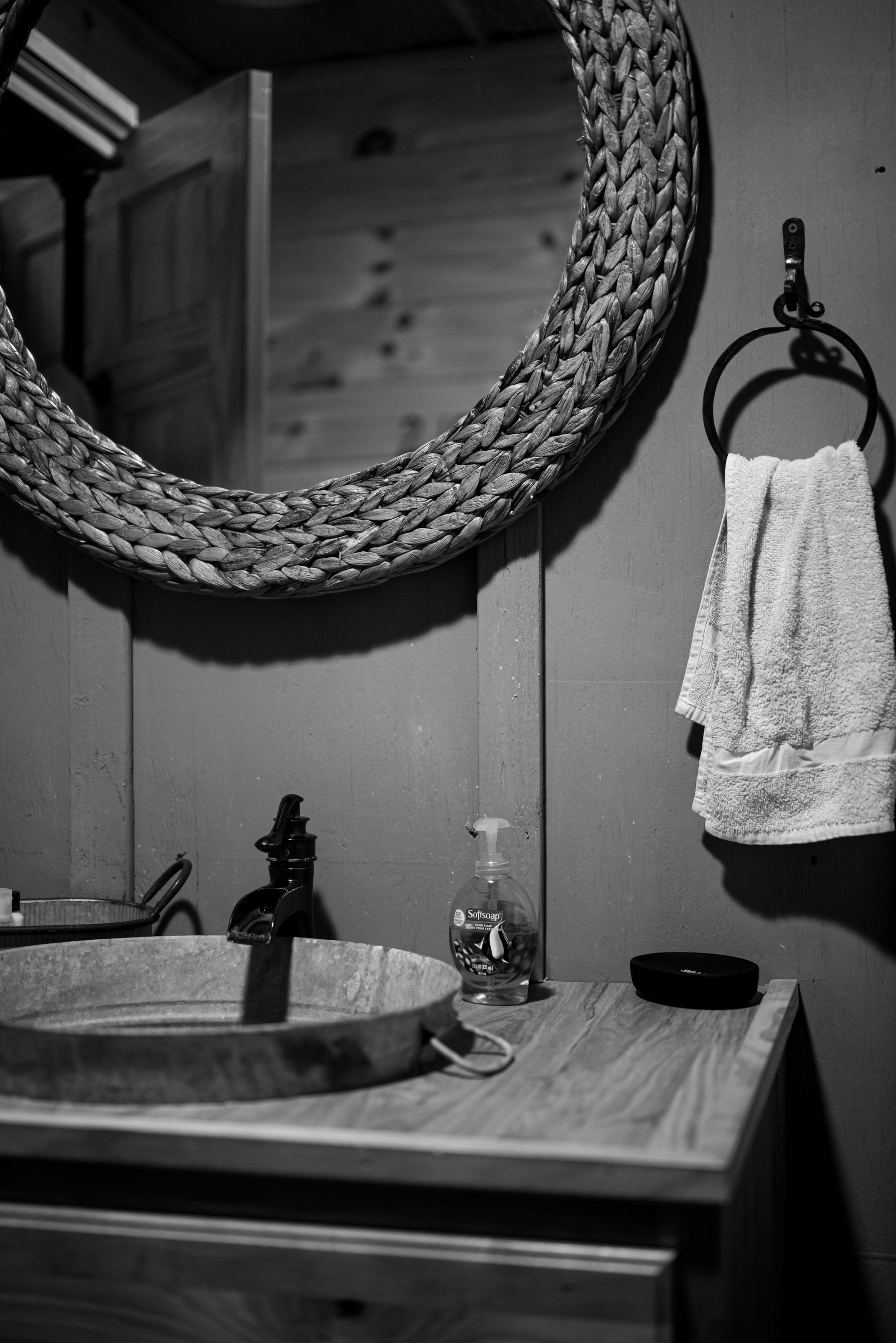 Black and white bathroom scene with woven mirror and rustic sink texture