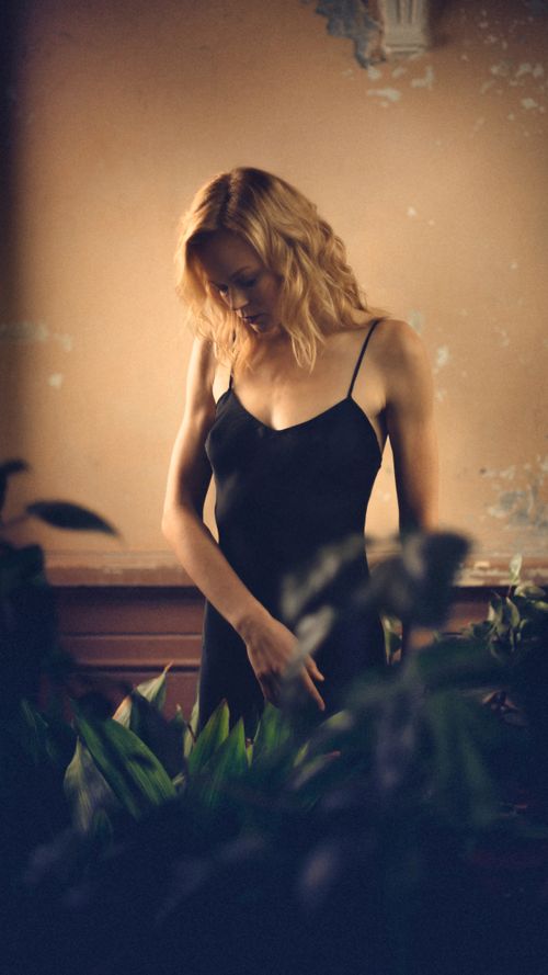 Free Caucasian woman in a black dress stands indoors surrounded by plants. Stock Photo