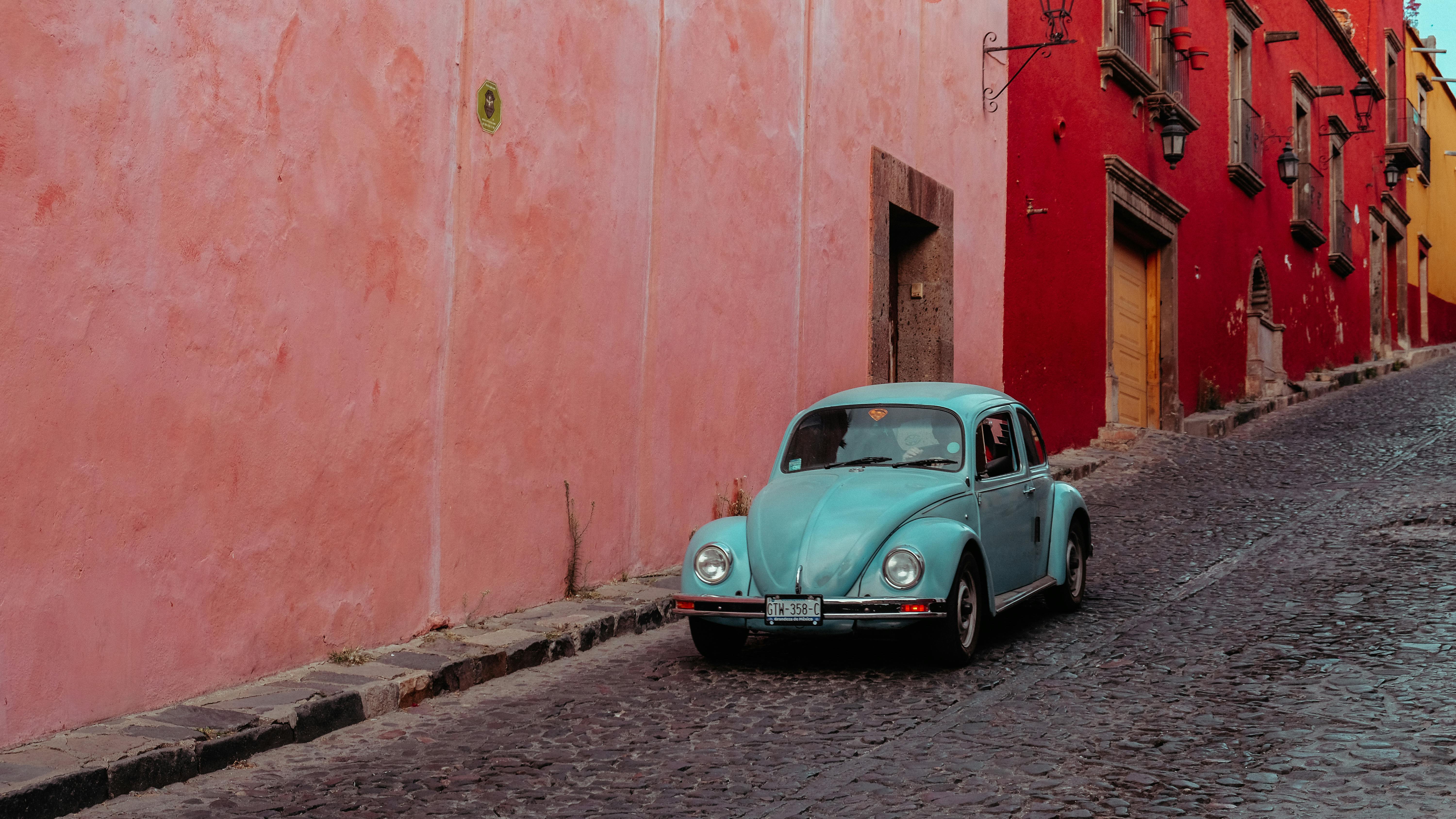 turquoise buggy moving along street with pink and red buildings