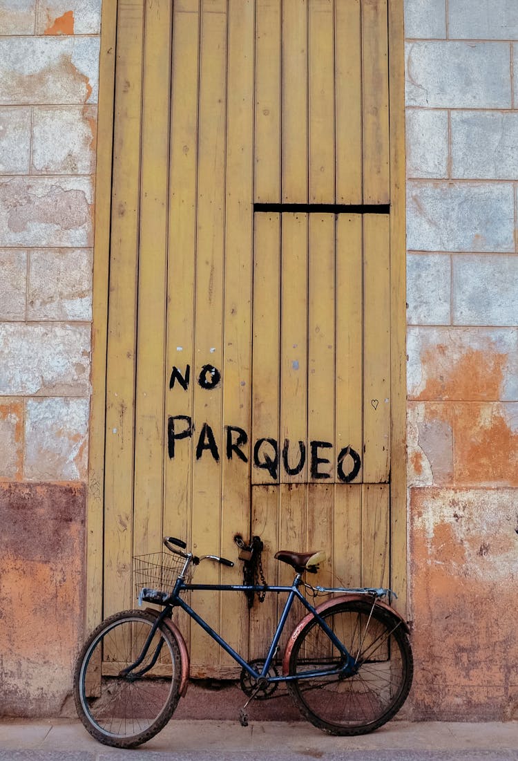 Bicycle Parked In Front Of A Wooden Door With Painted No Parking Sign