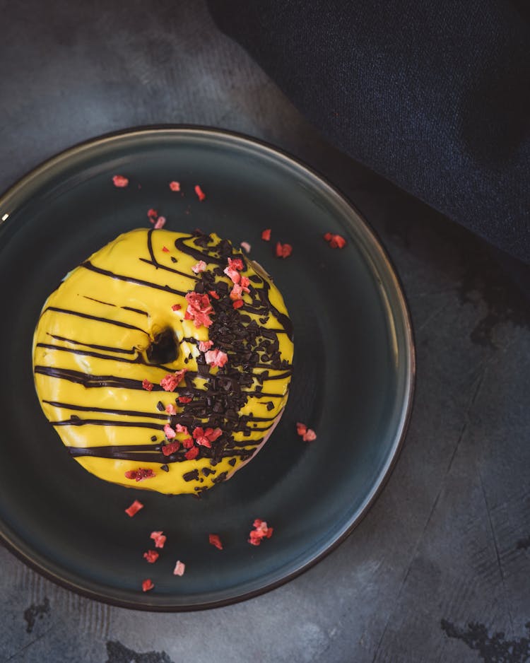 Donut With Yellow Icing And Chocolate Sprinkles On Ceramic Plate