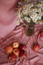 Red Apples in Metal Basket and Bunch of Flowers Laying on Pink Tablecloth