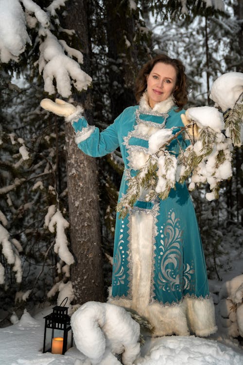 Woman in Blue Robe Standing Beside Snow Covered Trees
