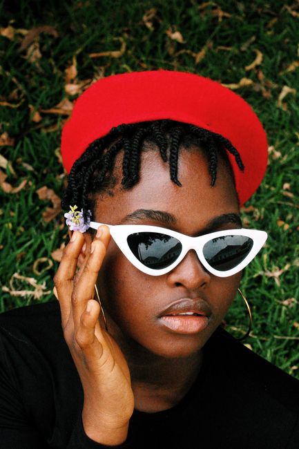 Portrait of a woman in a red beret with sunglasses, outdoors on grass.