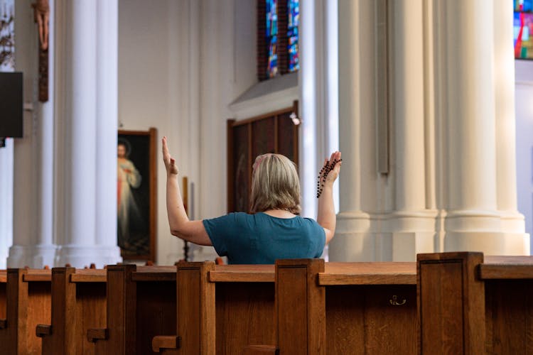 Woman In Church Pew Praying With Rosary In Hands Raised Above Head