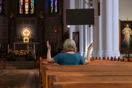 Woman Sitting in Church Pew Praying with Rosary in Hand