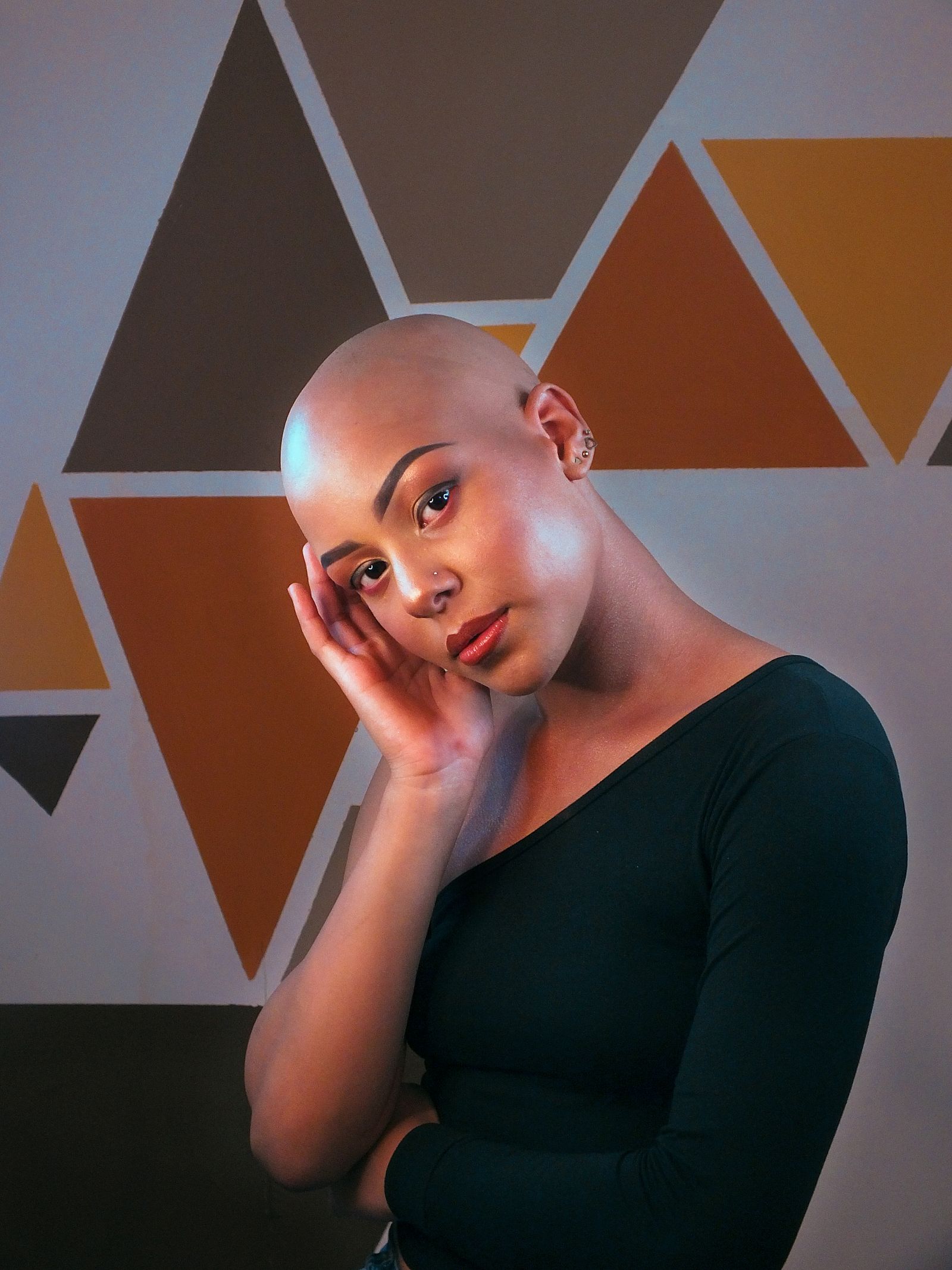Woman with a bald head resting one hand against her head
