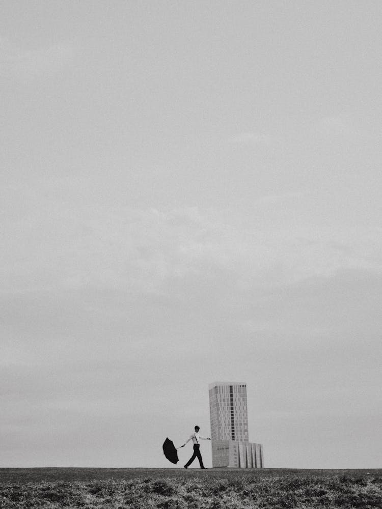 Man In White Shirt Walking In Field With Parasol By Unrecognizable Construction