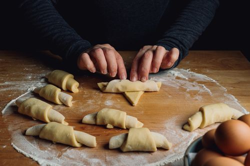 Free Close-up of hands rolling croissant dough on a floured wooden table indoors, showcasing pastry preparation. Stock Photo