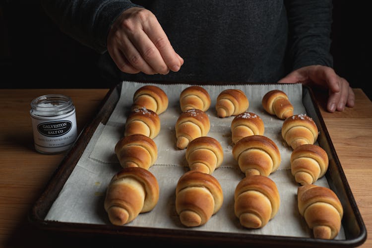 A Person Sprinkling Salt On Croissants 