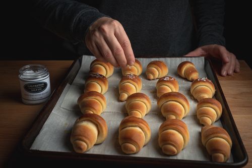 Free Artisan baker seasoning freshly baked croissants with sea salt on a tray. Stock Photo