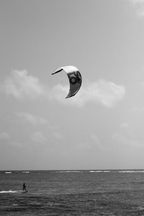 Grayscale Photo of a Person Kite Surfing in the Sea