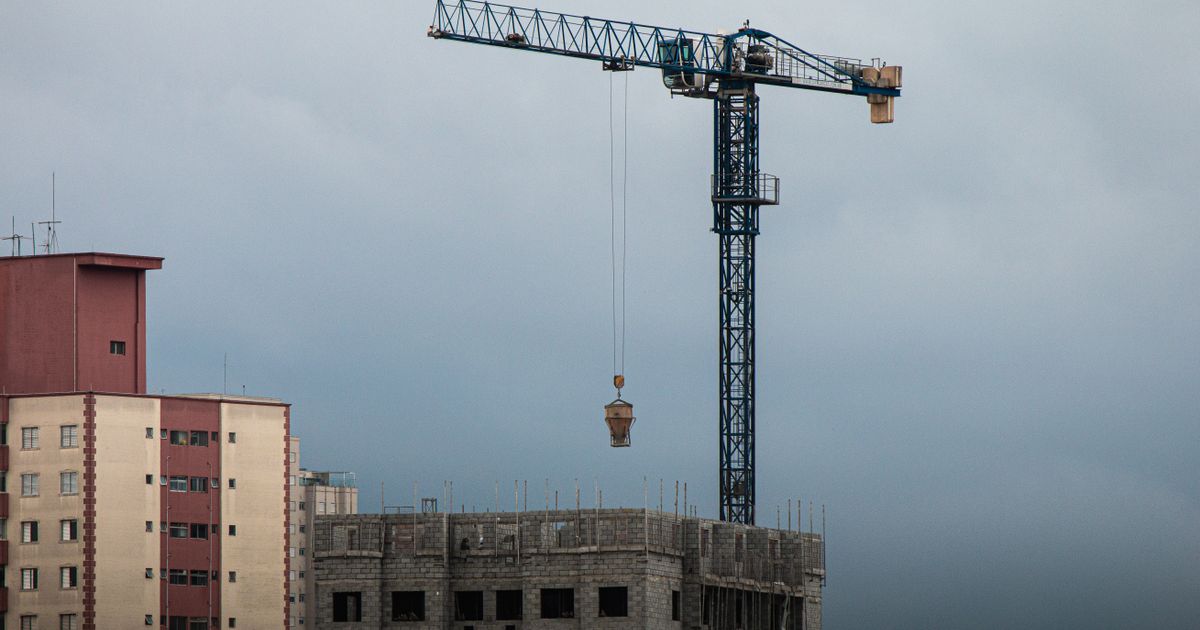 Canteiro de obras de alto prédio com um guindaste torre levantando materiais ao anoitecer.