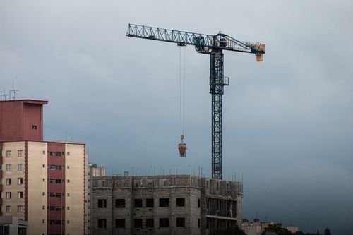 Free High-rise construction site with a tower crane lifting materials at dusk. Stock Photo