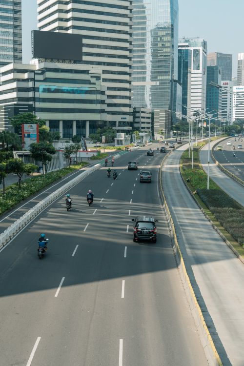 Free Aerial view of a bustling city avenue with cars and motorcycles surrounded by modern skyscrapers. Stock Photo