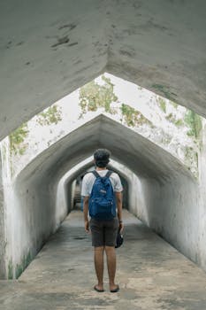 A man in a blue backpack stands in a historic arched tunnel, exploring the architecture.