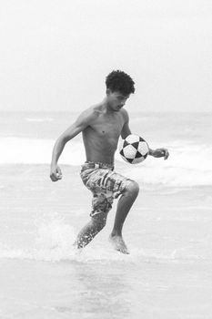 Black and white photo of a young man skillfully playing soccer on the beach.