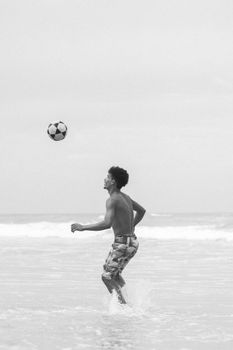 A man plays soccer on the beach, captured in a monochrome style, showcasing movement and athleticism.
