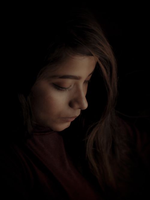 Free A thoughtful woman in a dark setting, captured in a side profile with soft lighting. Stock Photo