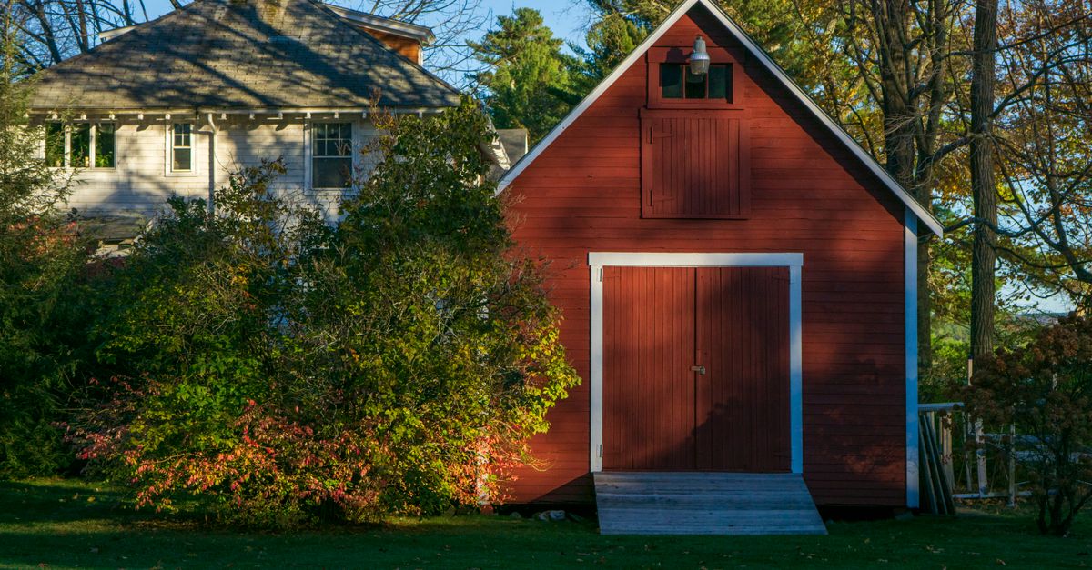 A picturesque red barn nestled amidst lush greenery on a sunny day, evoking rural tranquility.