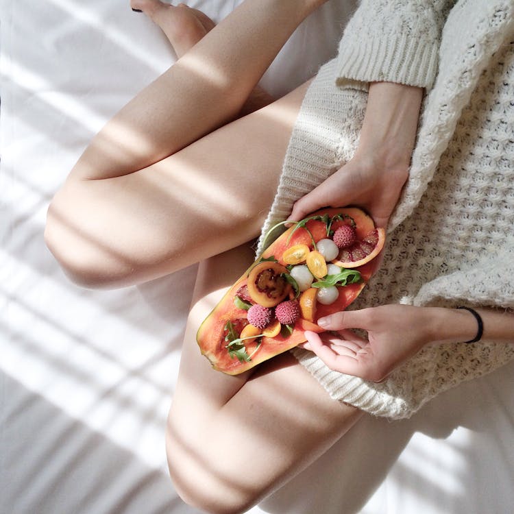 Person Holding Papaya Fruit on Bed