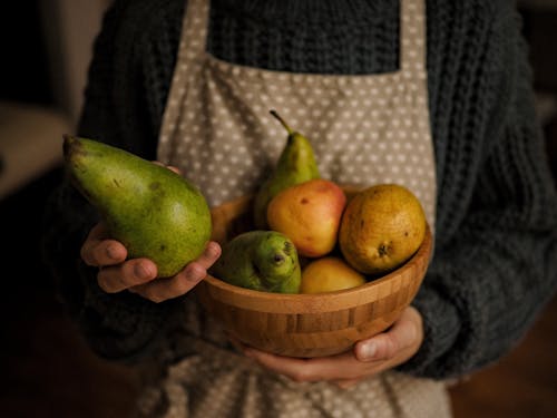 Photo of a Person's Hands Holding a Green Pear and a Wooden Bowl
