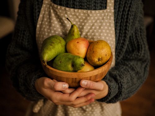 Free Close-up of hands holding a wooden bowl filled with pears and apples in warm indoor lighting. Stock Photo