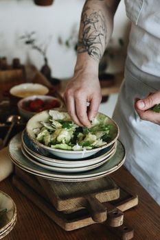Close-up of a tattooed hand preparing a fresh green salad in a bowl.