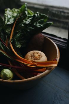 A close-up of fresh vegetables in a wooden bowl by a window, showcasing natural textures and colors.