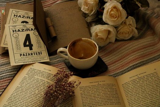 Aesthetic setup of coffee, books, and white roses on a cozy blanket.