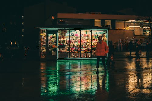 Person in Red Bubble Jacket Standing in Front of Store during Night Time
