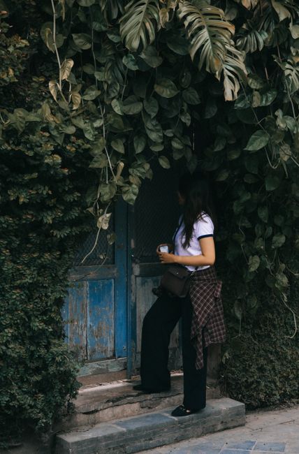 Young woman standing by a rustic blue door surrounded by lush greenery in Kotagede, Jogja.