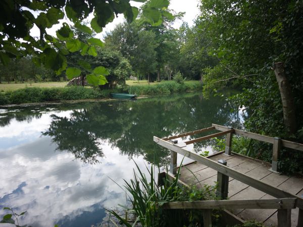 Ponton en bois et petite barque sur une rivière calme reflétant les nuages