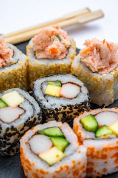 Close-up view of assorted sushi rolls with chopsticks on white background.