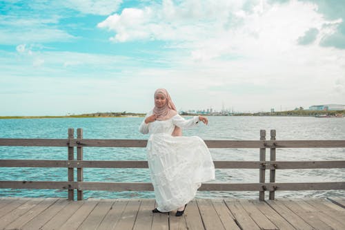 A Woman in White Dress Standing on a Wooden Dock