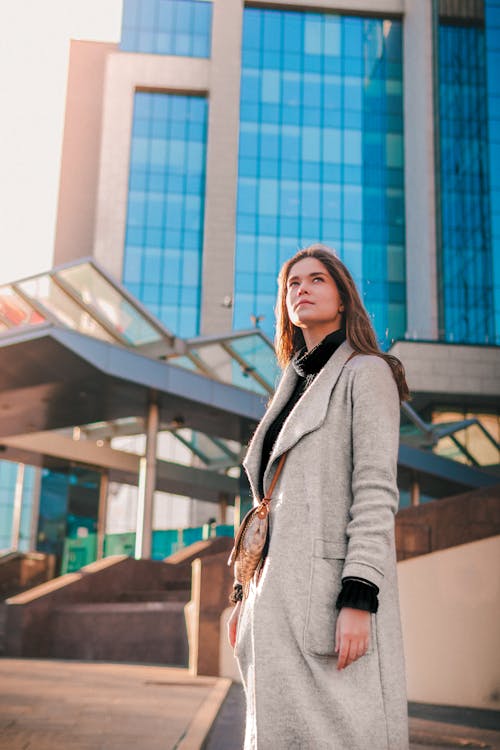 Free A Low Angle Shot of a Woman in Trench Coat Standing Near the Building Stock Photo