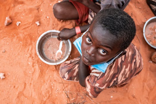 Child on a sandy ground in Luanda with mask and empty bowl, highlighting pandemic challenges.